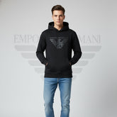 Man wearing a black Emporio Armani hoodie and blue jeans on a gray background